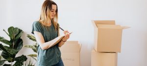a woman writting items down on her checklist with stack of boxes behind her