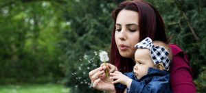 a mom blowing a dandelion with ther baby