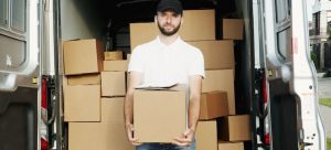 A professional mover standing in front of a loaded van, while holding a box;