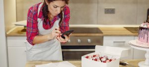 Woman making cakes and reading article on how to prepare your home for a New Year's Eve party, on her smart phone