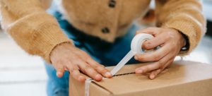 Crop unrecognizable woman sealing carton parcel with tape and knowing how to safely pack away seasonal items